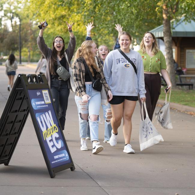 A group of excited students walking together, some raising their hands in celebration, during a UWmeetsEC event.