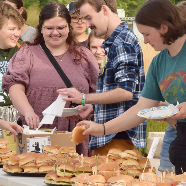 several standing students take sandwiches from platters