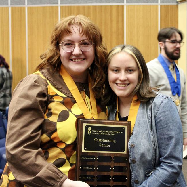 two graduating seniors smile with a plaque