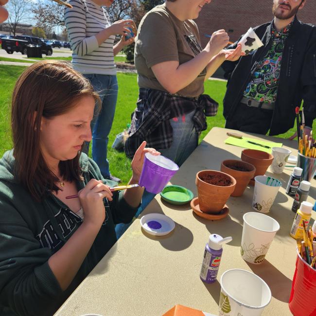 four students paint pots outside