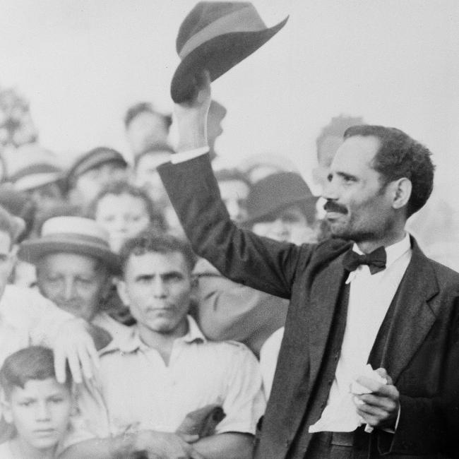 Black and white photograph of a man raising his hat to a crowd of onlookers.