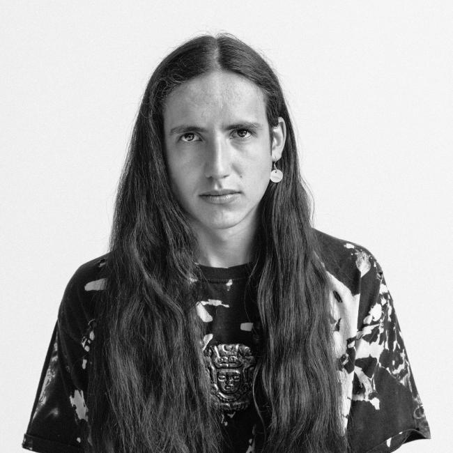 A black and white image of a person with long hair faces the camera.