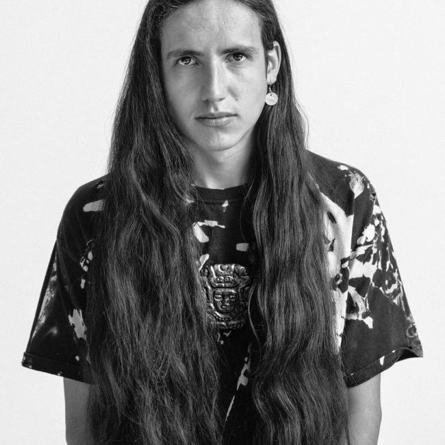 A black and white image of a person with long hair faces the camera.