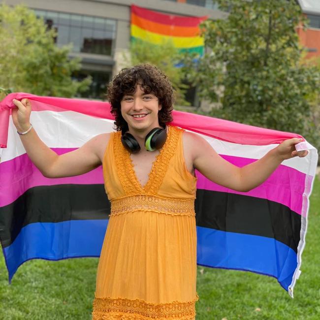 A person holding a pride flag smiles for the camera. 