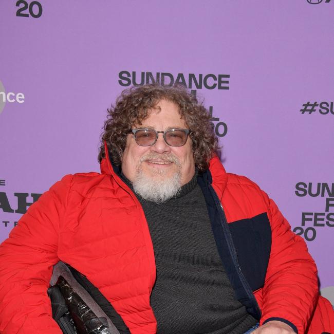 A man sitting in a wheelchair smiles for the camera. 