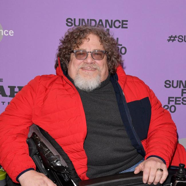 A man sitting in a wheelchair smiles for the camera. 