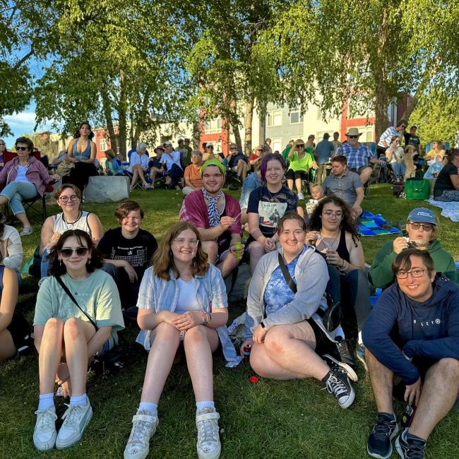 A large group of students smiles for the camera while sitting on a grassy hill.