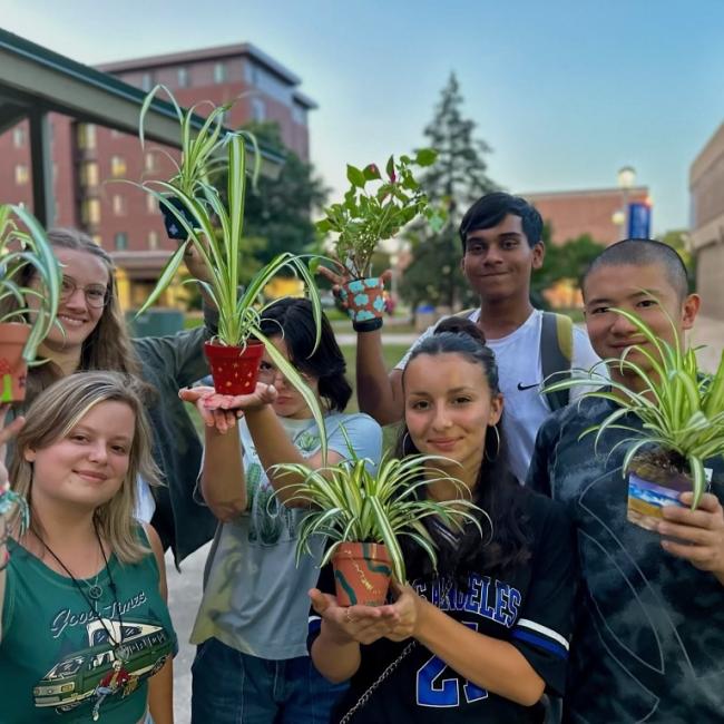 Students smile at the camera while showing off their small potted plants. 