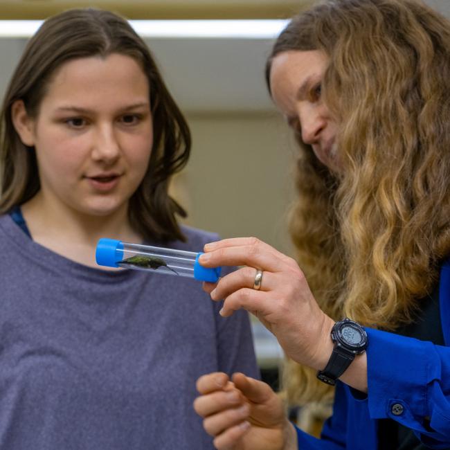 A student and professor study a very small bird in a test tube