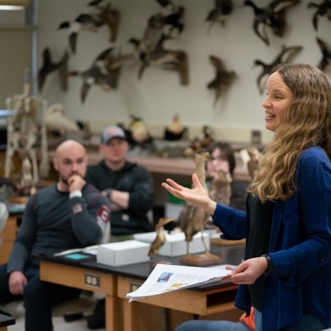 Professor speaks to a classroom of students surrounded by preserved birds