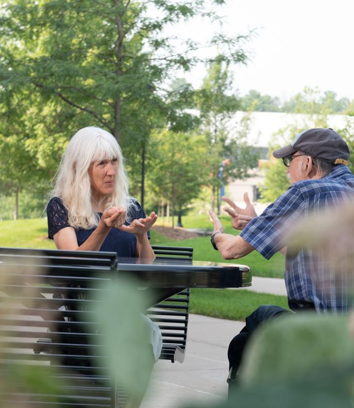 two people using sign language at a table outside 