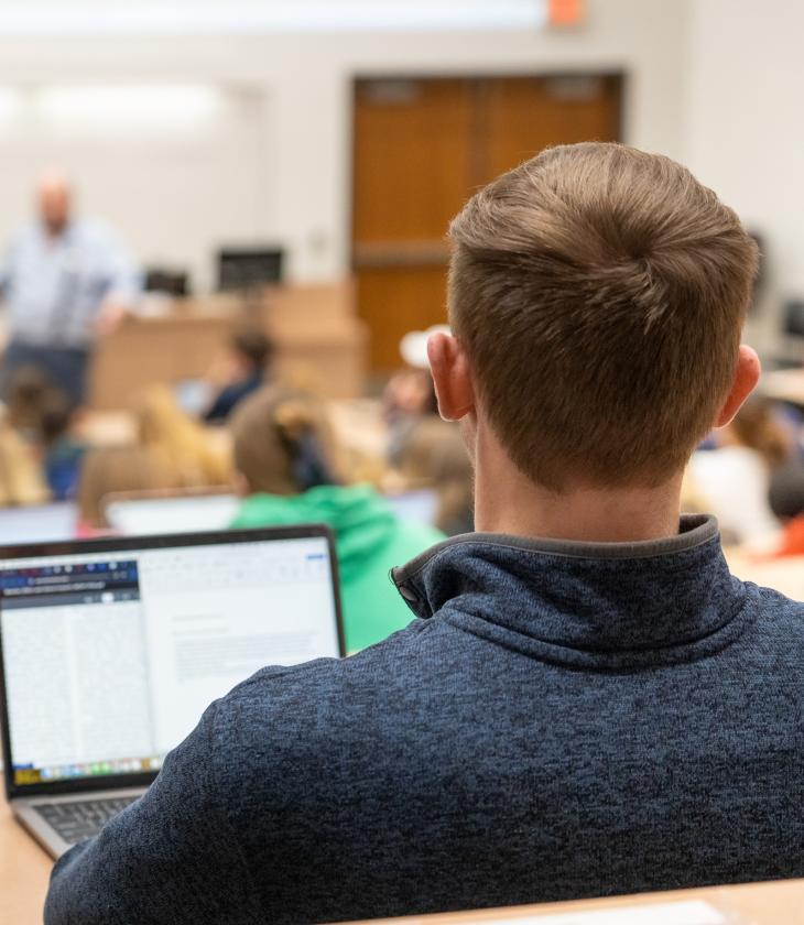 back of male student's head in classroom lecture, laptop open