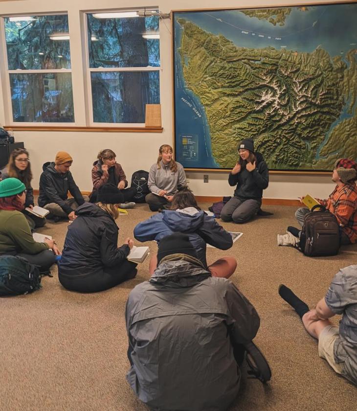 students seated on the floor in a national park center listening to guide