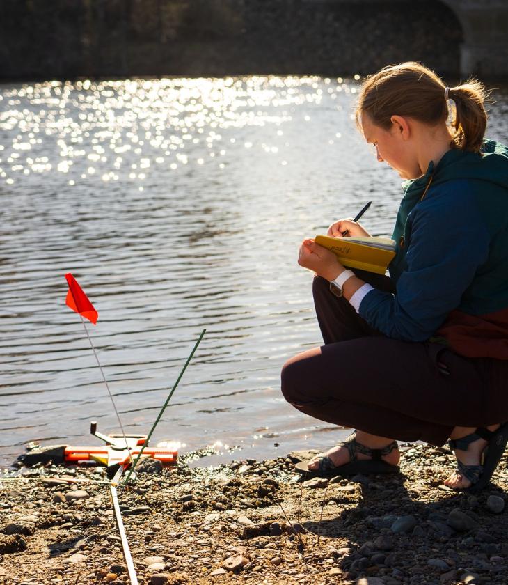 female student using geography instrumentation by the river bank 