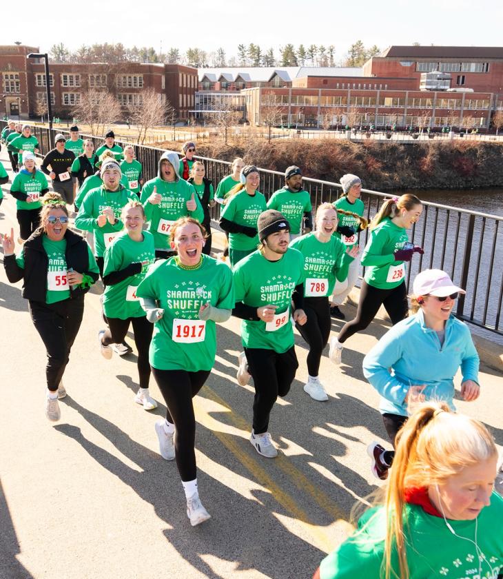 runners in green shirts crossing campus footbridge for a race 