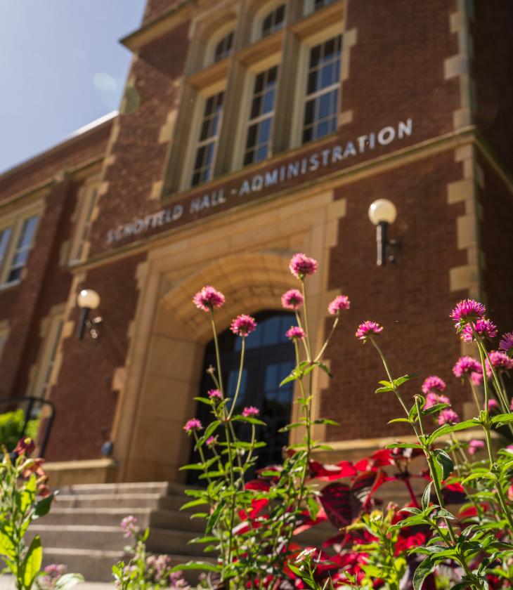 Pink flowers in front of Schofield Hall on a sunny day.