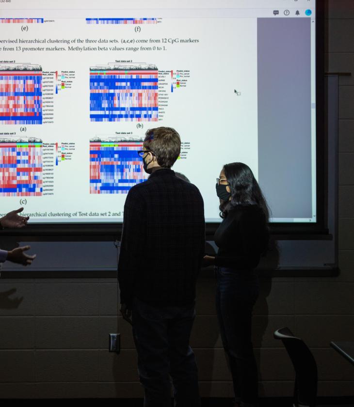 Computer science students standing in front of a projected image discussing