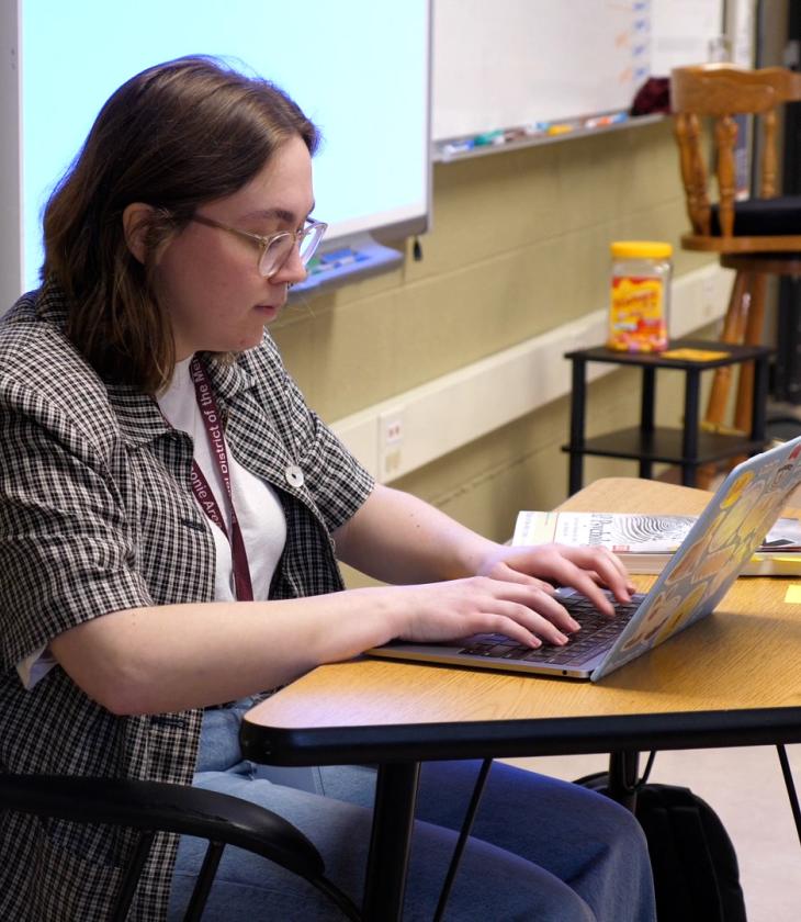 Teacher works at their laptop in a classroom setting