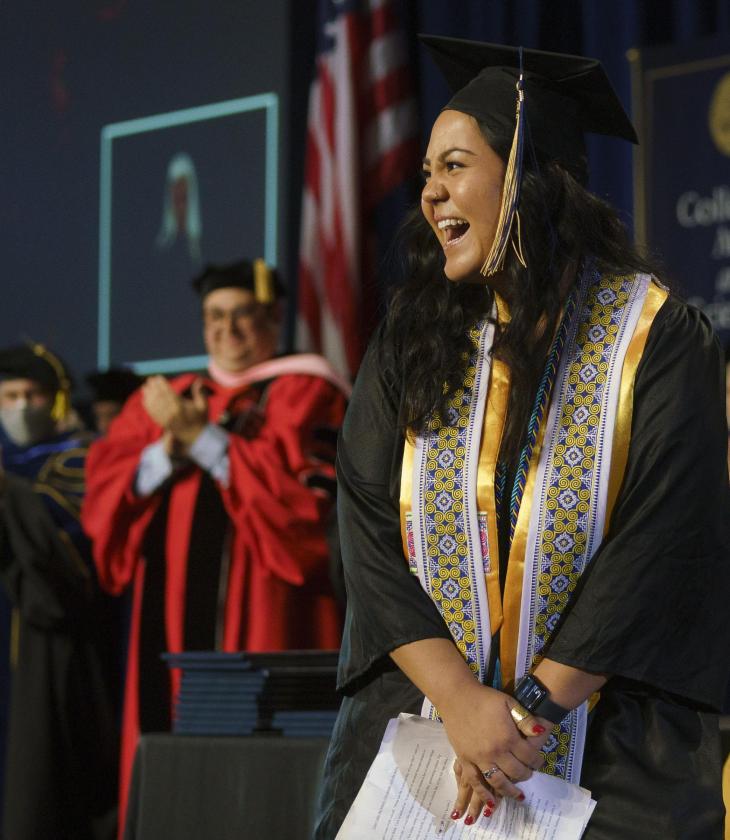 female student on commencement stage smiling at the crowd