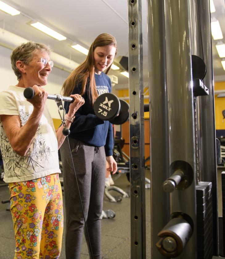 women lifting arms weights in McPhee fitness center with a female student assisting