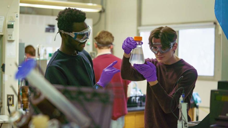 two male students in chemistry lab examining beaker 