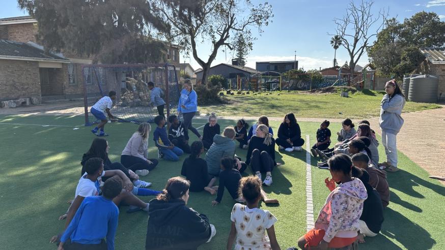 A group of people sit in a circle on grass on a sunny day