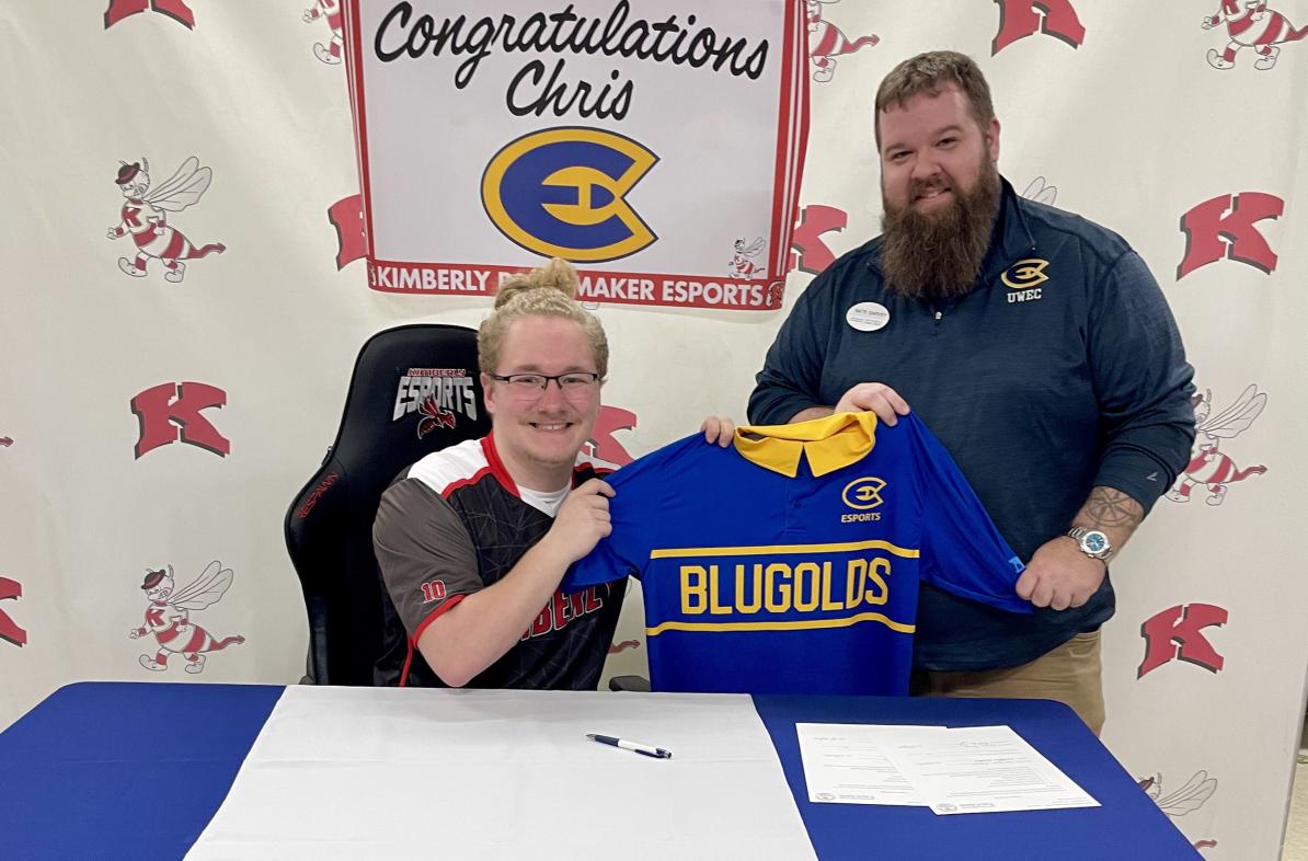 Two people pose for a photo at a table with the UWEC Esports logo.