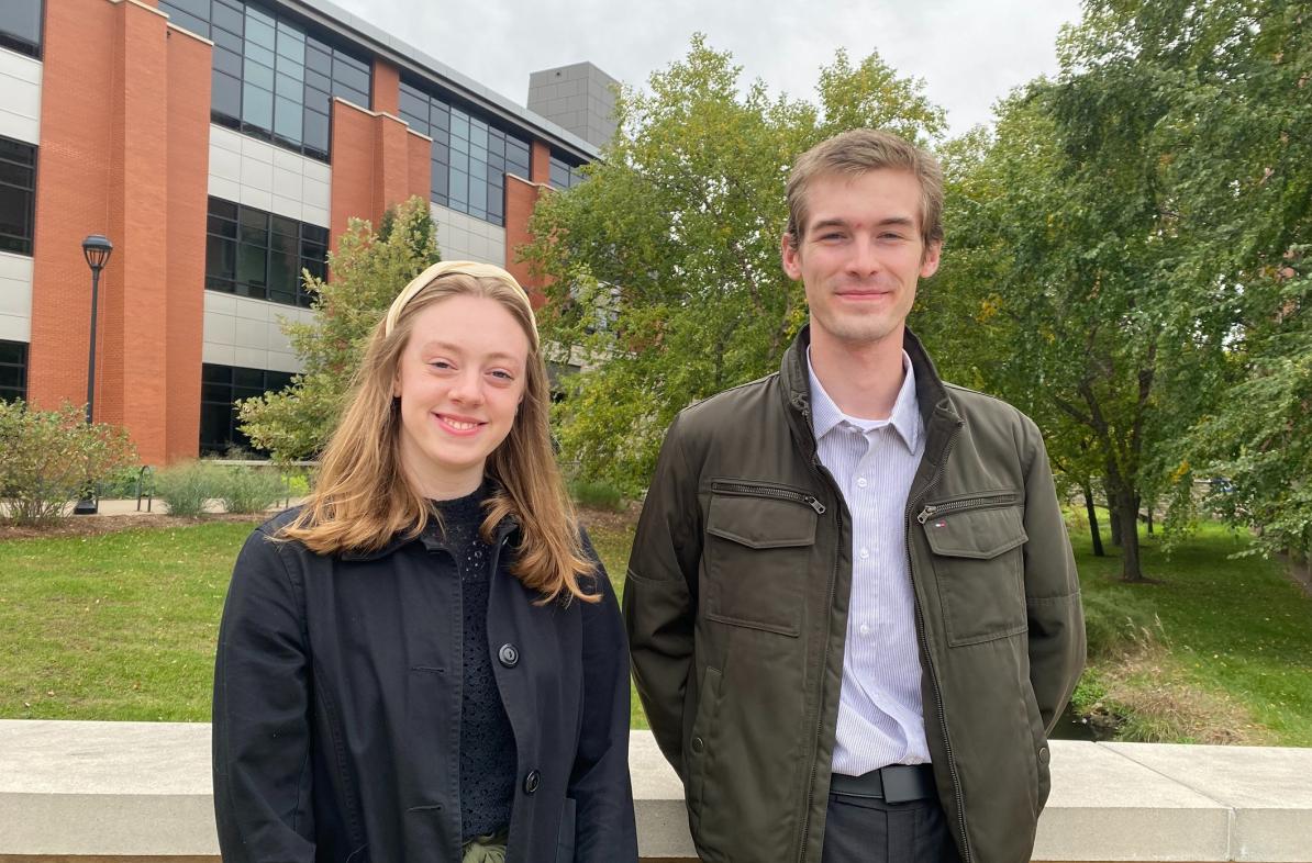 Two students in front of Davies, jackets on, standing on the bridge