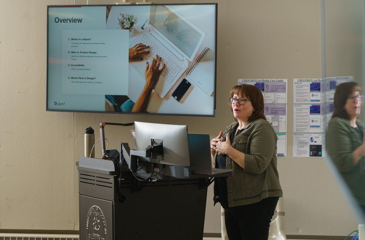 Woman in a classroom showing a Powerpoint on a screen.