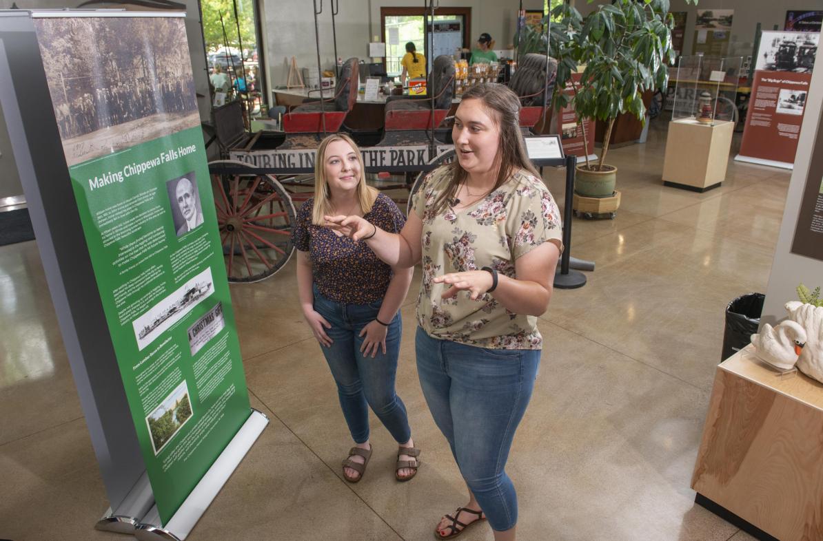 UW-Eau Claire public history graduate students Jordan Stish (left) and Alexi Linder discuss the exhibit they helped create in the Irvine Park Welcome Center in Chippewa Falls. (Photo by Shane Opatz)