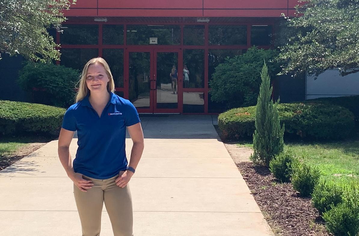 female student standing in front of commercial building, blue shirt says Rust-Oleum