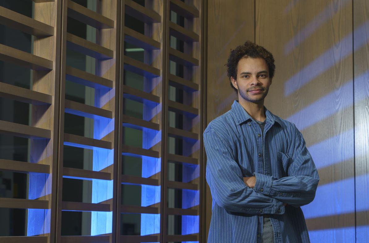 Cameron Merline, male student standing in front of decorative wall divider