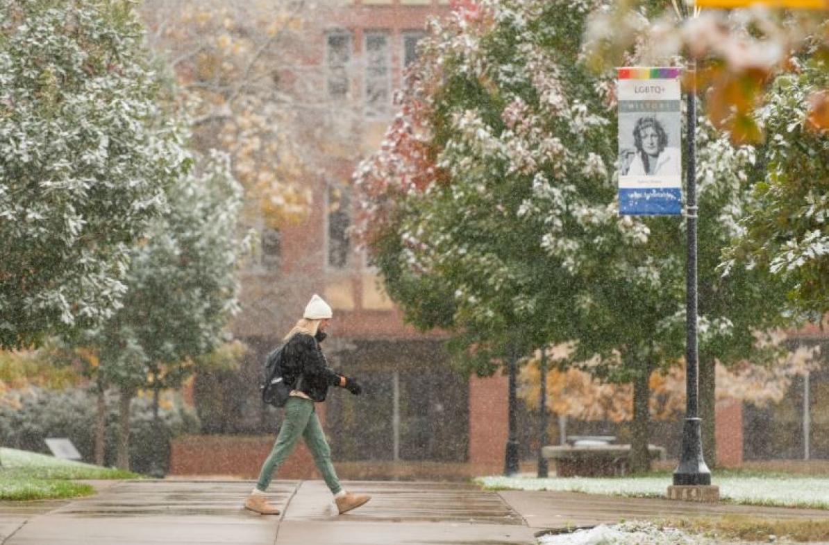 College students walking past building while snow is falling.