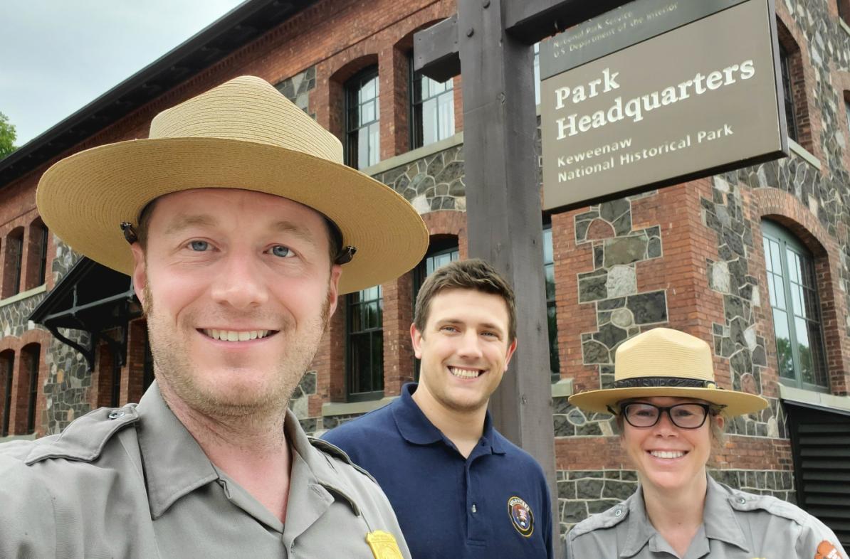 Two National Park Service staff in uniform and one Blugold student outside of a historic building in Michigan