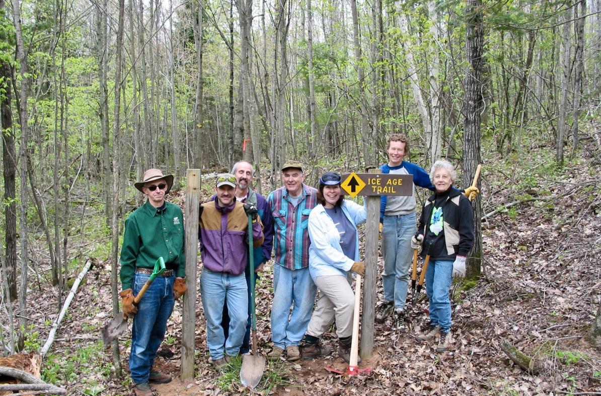 Group gathers for a photo in the woods by sign that reads "Ice Age Trail."