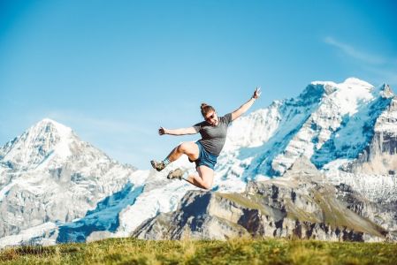 student jumping into the air in Sweden, snowy mountains behind