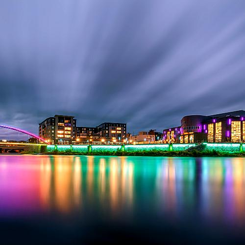 Pablo Center as viewed from across the river at night with the bridge lit up.